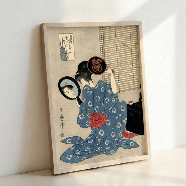 Serene framed poster of a geisha applying makeup at her mirror, executed in the Japanese woodblock style with a refined palette of cream, pale blue, and deep indigo.