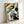 Japanese woodblock print of a geisha adorned in patterned kimono with parasol, composed in muted yellows, teals and warm cream hues.