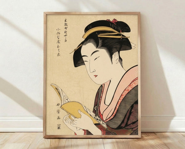 Elegant Japanese woodblock print of a geisha in a red kimono reading a book, rendered in cream, black, and gold tones with serene Edo period aesthetics, displayed as a framed poster on a wall.