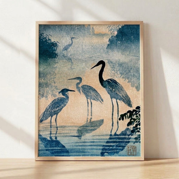 Serene Japanese woodblock-style poster featuring herons in a misty wetland landscape with bamboo and forest elements in slate blue, cream, and charcoal tones, framed on wall.