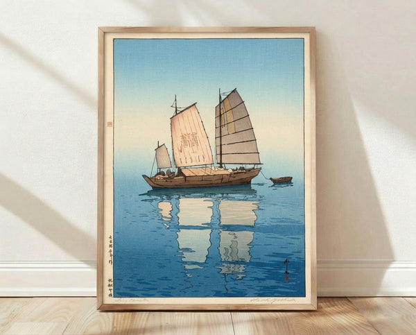 Japanese woodblock print of a sailing junk with billowed sails reflected in calm blue water, rendered in serene coastal tones of cream, grey, and pale yellow.