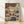 Oni mask with demon face in burnt orange and navy blue, surrounded by autumn maple leaves and swirling clouds in Japanese woodblock style, framed poster on wall