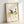 Framed wall art depicting a rooster in traditional Japanese woodblock aesthetic, combining decorative linework with subtle teal and rust accents on cream.