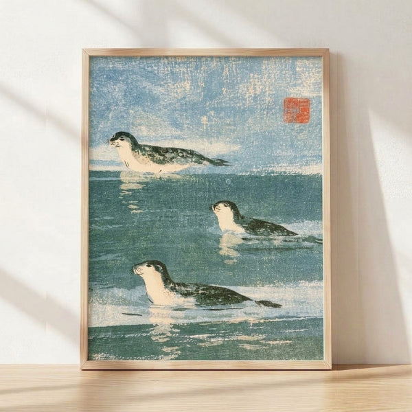 Framed Japanese woodblock-style print featuring seals swimming in tranquil water rendered in dusty blue, dark teal, and cream tones, evoking a serene and naturalistic mood.
