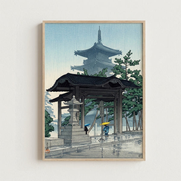 Vintage-style framed poster of Tsuchiya Koitsu's rain scene, showing a peaceful pagoda entrance with lanterns and contemplative figures in soft cream and navy palette.