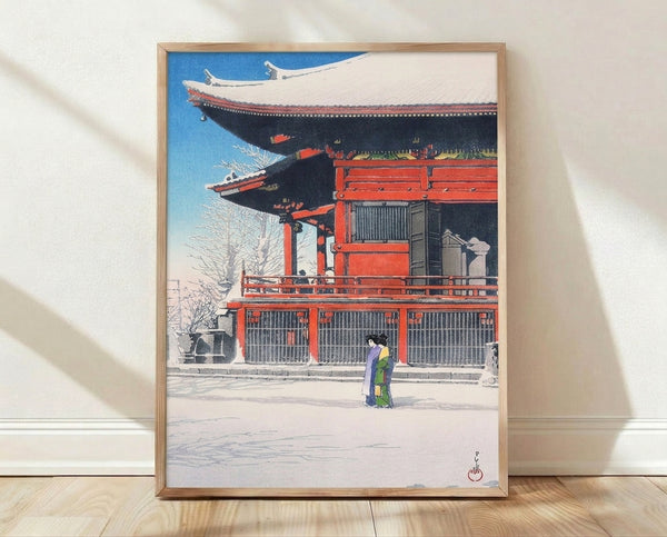 Serene Japanese woodblock print featuring a woman in a crimson kimono standing before a snow-covered temple, rendered in cerulean blue, cream, and charcoal tones, framed as wall art.