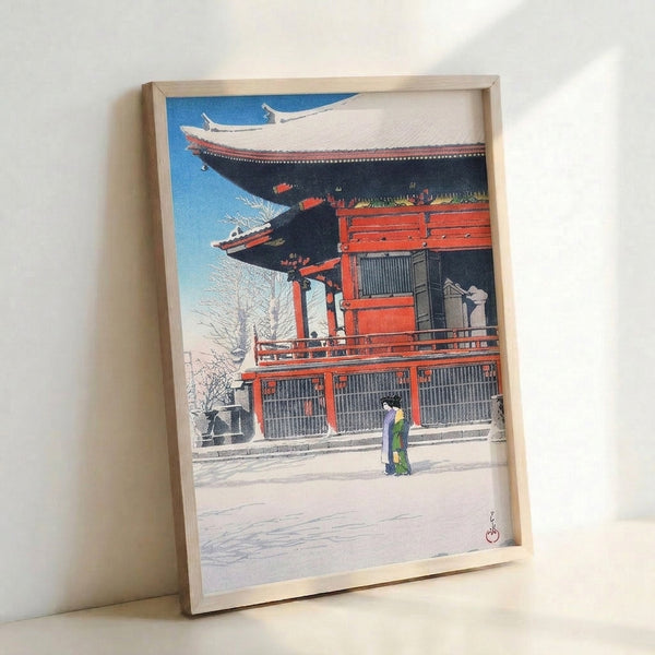 Framed Japanese woodblock print showing architectural temple details and a kimono-clad woman amid falling snow, using rich cerulean, deep black, and cream accents for serene mood.
