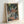 Framed Japanese temple woodblock print depicting the atmospheric entrance to Nikko Toshogu shrine with forest greens, sky blue sky, and a solitary monk among ceremonial elements.