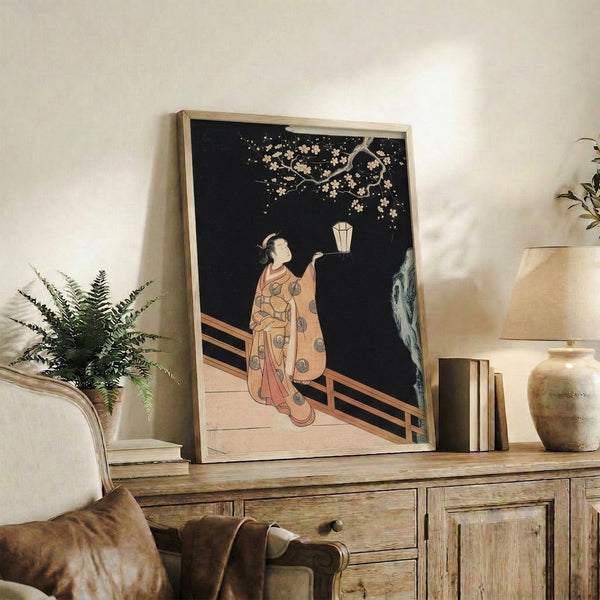 Framed wall art in Japanese woodblock tradition: robed woman with lantern beneath hanging cherry tree, evoking quiet nighttime beauty in cream, gold, and pale blue.