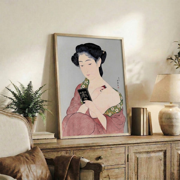 Framed Japanese-style portrait of a refined woman in patterned crimson kimono examining herself in a hand mirror, rendered with traditional woodblock technique and sophisticated gold detailing.