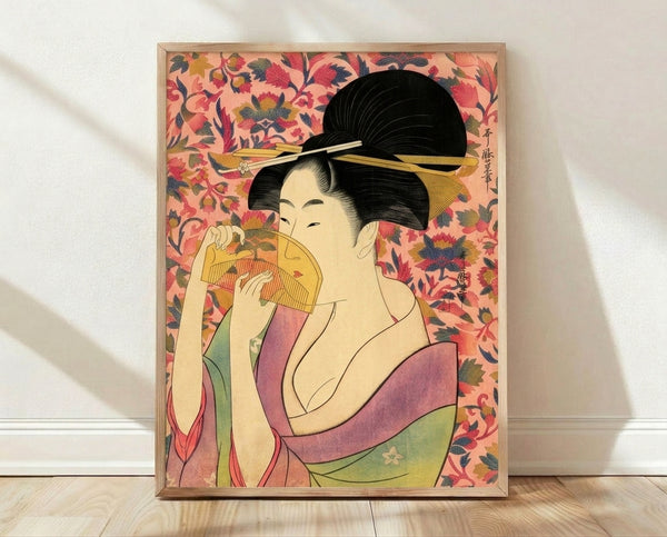 Framed Japanese woodblock print of an elegant geisha in a coral pink and gold kimono, holding a decorative fan with contemplative expression amid soft florals and mauve tones.