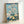 Framed vintage-style woodblock poster of Mount Fuji surrounded by cherry blossoms, rendered in muted prussian blue, pale yellow, and cream with a meditative atmosphere.