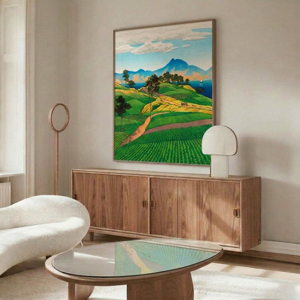 Framed Japanese woodblock-inspired poster capturing a serene pastoral landscape with rolling green fields, distant peaks, sailboat, and layered sky in soft cream and blue hues.