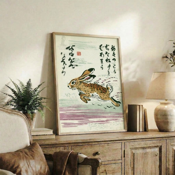 Whimsical framed art print in Japanese woodblock style showing an energetic leaping rabbit in soft cream and mauve, complemented by bold calligraphy in dark green.
