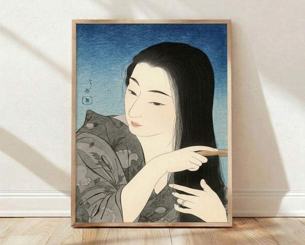 Serene Japanese woodblock print framed on wall depicting a woman in traditional kimono combing her hair, rendered in elegant blue, black, and cream tones with contemplative mood.