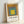 Framed poster art displaying nested rectangular forms in muted ochre, gray, and teal with yellow accents in a Bauhaus minimalist style.