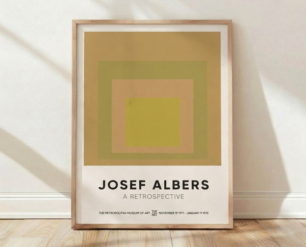 Framed Bauhaus art print featuring nested squares in gold, olive green, peach, and chartreuse yellow on a gallery wall.