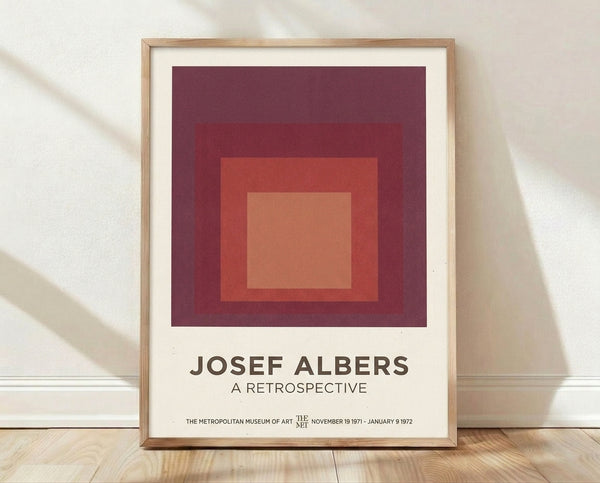 Framed minimalist poster featuring nested squares in warm tones of maroon, coral, and cream, exemplifying Bauhaus color theory and geometric abstraction.