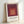 Structured geometric poster displaying layered squares in maroon, coral, and cream, reflecting the systematic color exploration central to Albers' artistic practice.