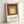 Framed mid-century abstract print with layered squares in muted burgundy, green, and pale yellow on a gallery wall.