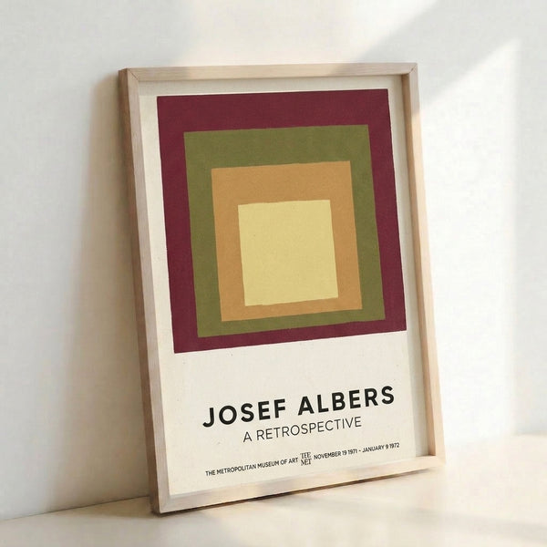 Framed mid-century abstract print with layered squares in muted burgundy, green, and pale yellow on a gallery wall.