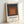 Abstract square composition in muted charcoal, terracotta, and tan layered concentrically, a modern minimalist poster print hung as framed wall art.