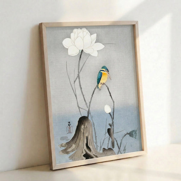 Serene botanical art print in Japanese tradition showing a poised kingfisher with white lotus flowers and delicate foliage in soft cream and blue tones on a wall.