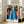 Contemplative wall art print with a blue-robed woman in an elegant interior space, abstract door frame opening to coastal view, palm motifs, and a palette of gold, terracotta, and cream.