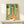 Mid-century modern framed wall art depicting a cheerful giraffe in an interior courtyard with lush potted plants and an arched doorway in warm retro colors.