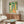 Retro giraffe artwork in art deco style showing the animal gazing upward through a decorative archway with surrounding houseplants in golden yellow, forest green, and coral tones.