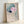 Framed Japanese-inspired watercolor print showing a graceful lotus with a songbird, composed in soft cream, sage green, and teal pigments with a meditative aesthetic.
