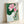 Framed poster depicting a graceful lotus flower in soft pink tones surrounded by green foliage, created in the style of Japanese woodblock art with delicate line details and cream background.