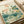 Contemplative botanical watercolor artwork depicting a tranquil pond scene with pink water lilies, koi fish, and a delicate dragonfly set against soft teal and cream hues.
