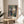 Peaceful interior scene poster in impressionist style: woman focused on needlework amid indoor plants near bright window light, rendered in soft blue, warm brown, and sage tones.