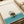 Modern art print featuring a tranquil figure in boots reading newspaper during a flood, minimalist composition in cream, tan, teal, and muted red.