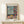Modern art print depicting a peaceful room interior with decorative curtains, potted plants, and a fruit bowl arrangement in warm and cool color harmony of cream, red, and green.