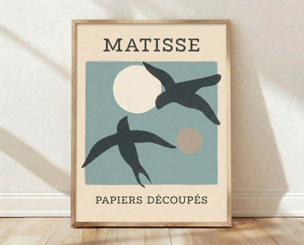 Framed abstract bird and moon poster in dusty blue, cream, and charcoal black, inspired by Matisse's minimalist cut-paper style with serene, playful sophistication.