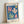 Cheerful abstract composition of overlapping circles and leaf-like shapes in golden yellow, deep blue, and sage green, presented as a framed mid-century print.