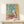 Intimate table arrangement poster depicting aubergines, pitcher, and plate amid vibrant foliage in warm coral and cool blue tones, framed wall art.