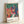 Framed modernist poster showing a woman musician with lush emerald foliage and warm coral-red details in Matisse's The Music composition.