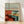 Retro mid-century poster art depicting a diner booth with red vinyl seating, turquoise accents, and a window view of sandy desert landscape; cream and sage green tones create a nostalgic Americana aesthetic.