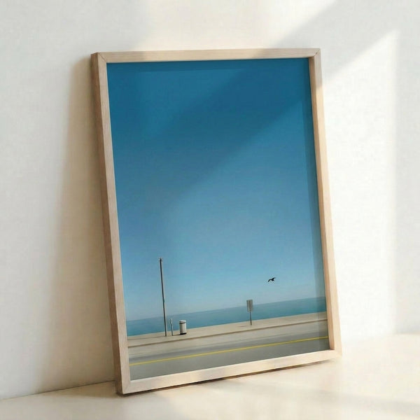Calm ocean-inspired wall art in modern minimalist style depicting a peaceful beach with a bird, pole, and trash can against soft blue and beige hues.