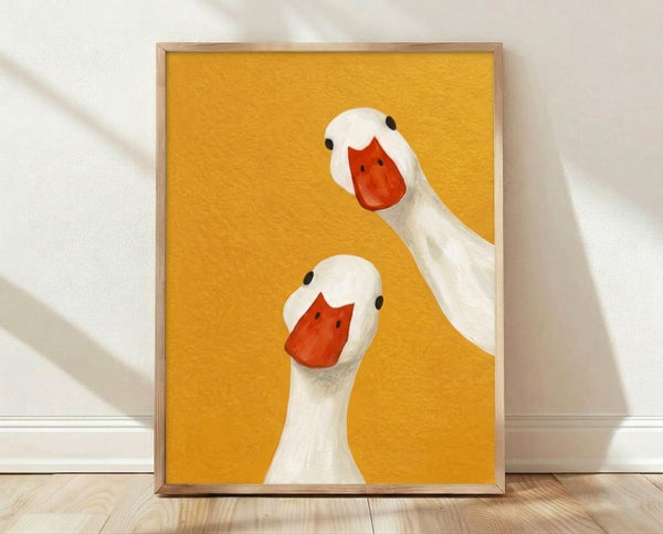 Minimalist framed poster of two playful geese with golden yellow and red-orange accents on a white background, modern art print with whimsical charm.