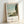 Framed impressionist art print depicting a peaceful riverside with boats, trees in muted greens, and a gentle blue sky creating a serene atmosphere.