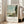 Soft-hued impressionist painting of sailboats anchored on water surrounded by green vegetation, a path, and distant church, evoking quiet contemplation.