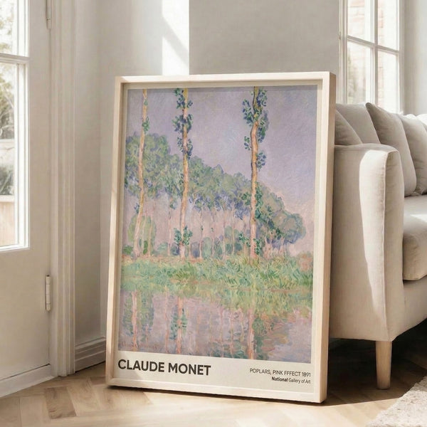 Atmospheric impressionist scene of poplar trees and their water reflections in soft pink, lavender, and yellow, displayed as a framed poster on interior wall.