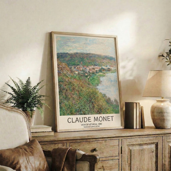 Framed Impressionist print of a serene village scene at water's edge, with layered hills rendered in tender shades of green, blue, and warm terracotta tones.