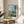 Impressionist poster art of a serene village landscape featuring vertical poplar trees, wildflower field, and distant buildings bathed in soft natural light and cloudscapes.