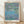 Soft impressionist painting of water lilies floating on a tranquil pond surrounded by lavender and blue tones, framed as a poster on a wall.