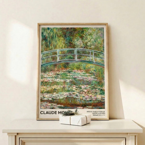 Framed impressionist artwork of Monet's famous Japanese bridge crossing calm waters dotted with water lilies, featuring a soft, hazy color palette of blues and ochres.